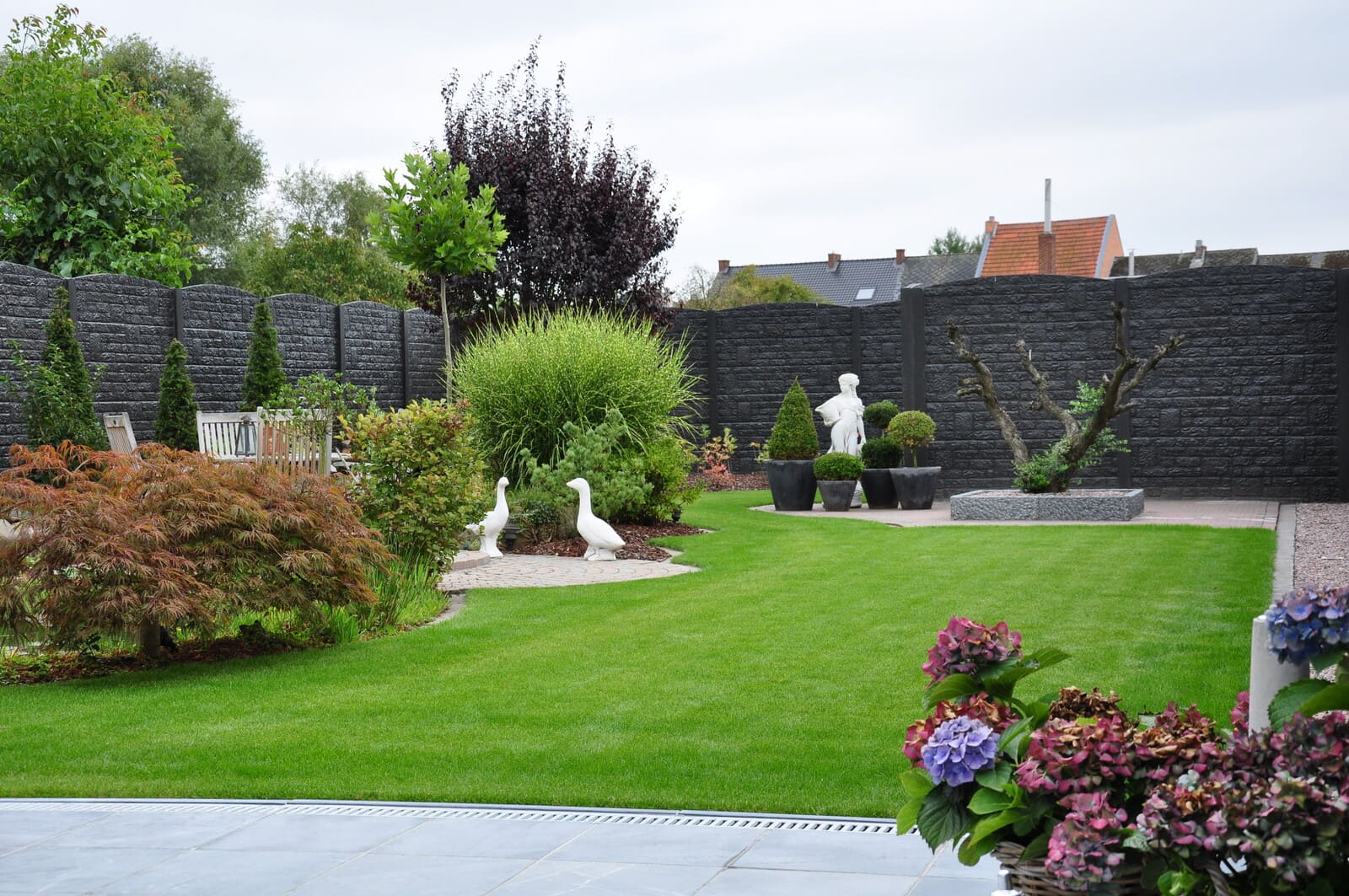 Großer Garten mit Kübelpflanzen, Kiesgruben und Skulpturen umzäunt mit einem dunklen Zaun